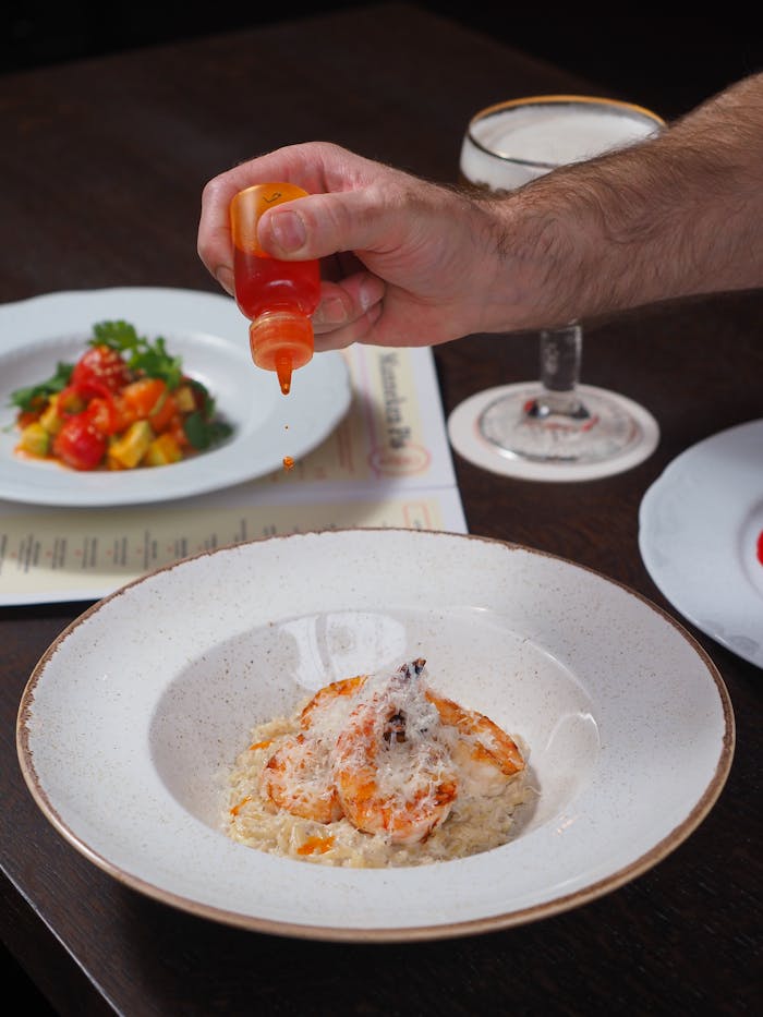 Close-up of a seafood dish being garnished with hot sauce, showcasing fine dining presentation.
