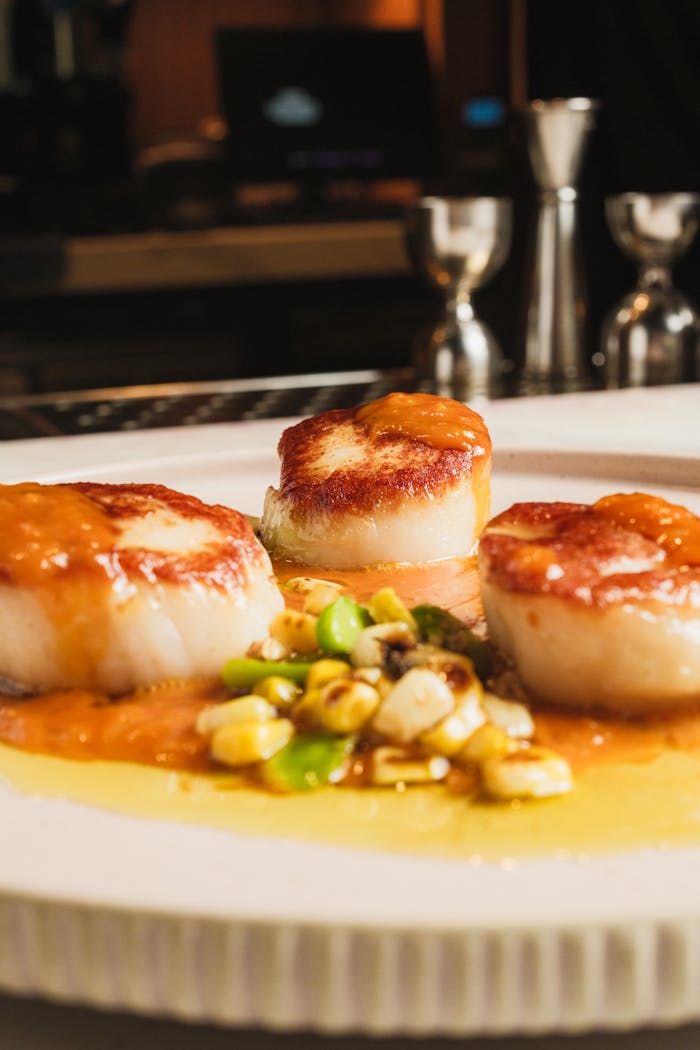 Gourmet seared scallops served with a savory corn succotash on a white plate.